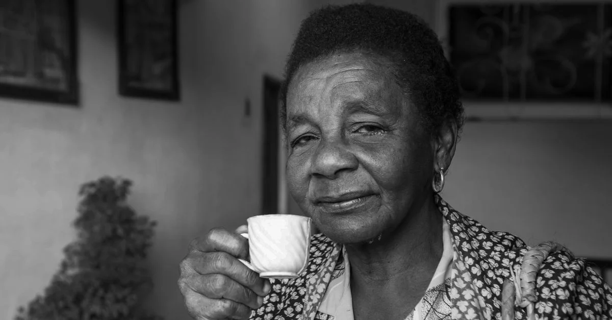 Portrait noir et blanc d'une femme senior tenant une tasse de thé à l'intérieur.