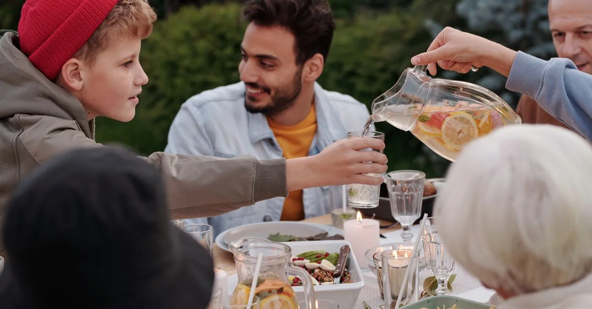 Une famille diverse profitant d'un repas extérieur partagé avec des boissons à la lumière du jour, favorisant la connexion et le bonheur.