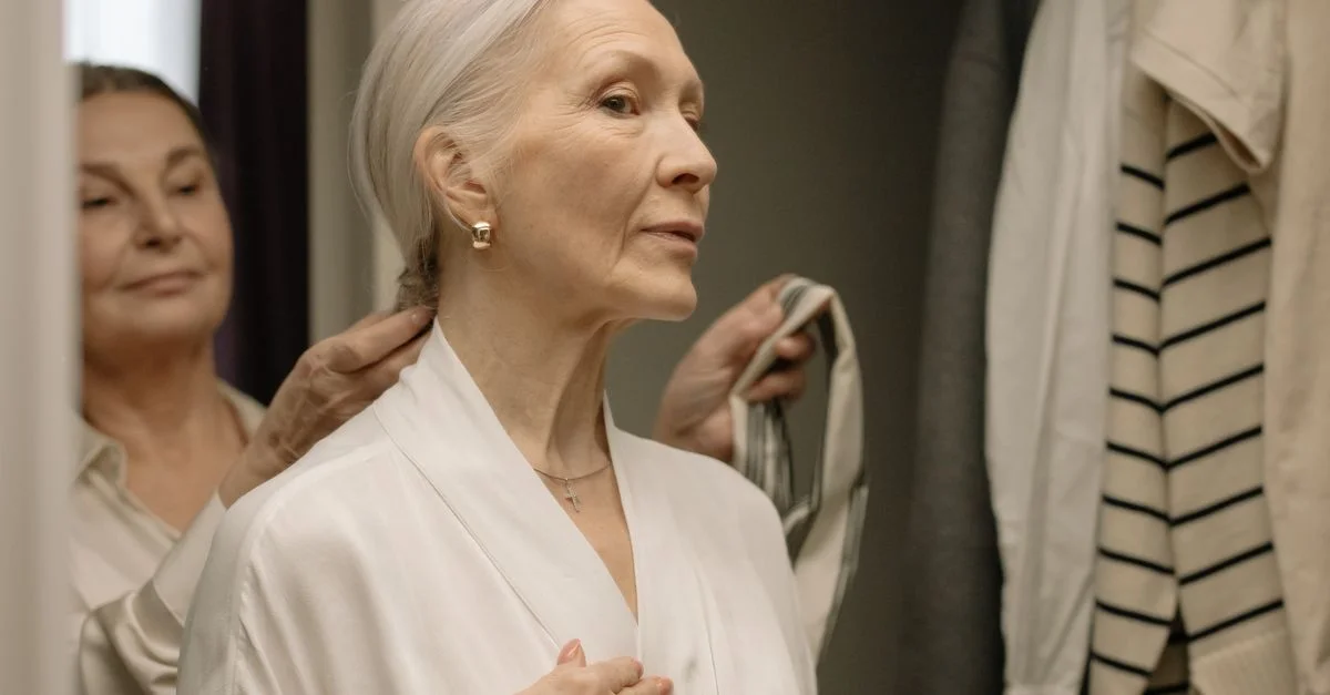Femme senior raffinée ajustant ses cheveux tout en portant un peignoir blanc à l'intérieur.