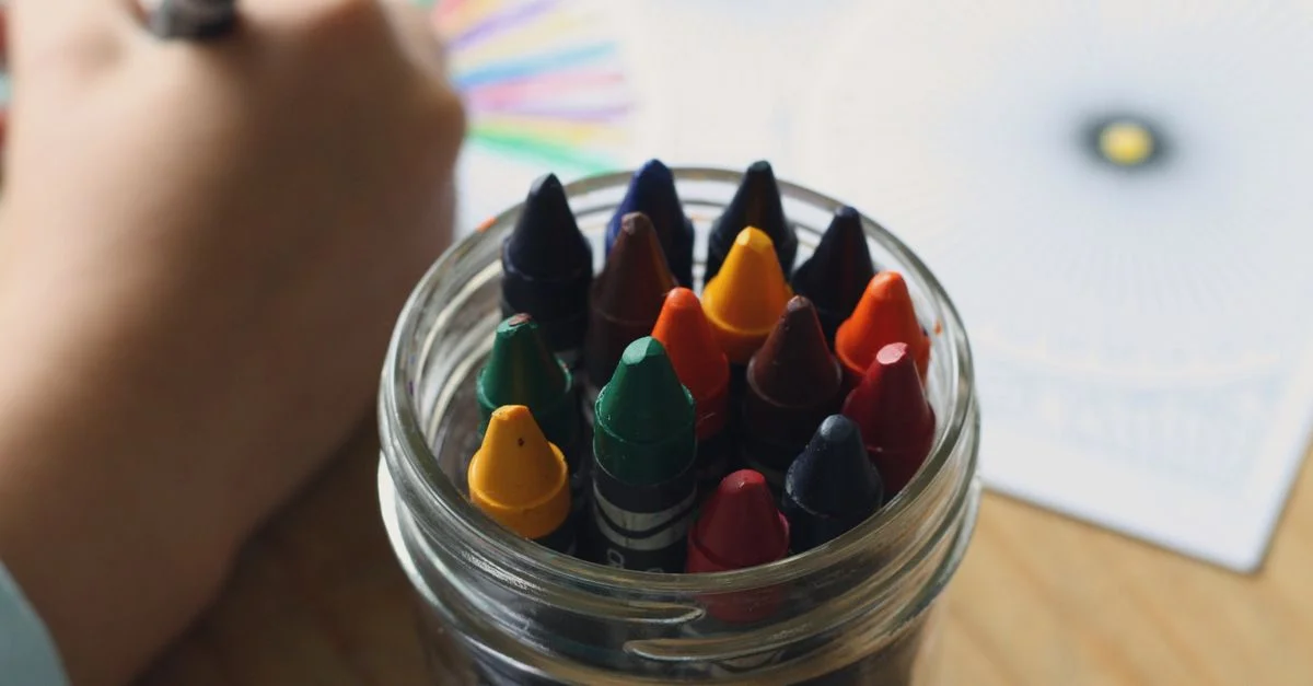 Un enfant coloriant avec des crayons dans un bocal, mettant en avant la créativité et le plaisir dans les activités artistiques.