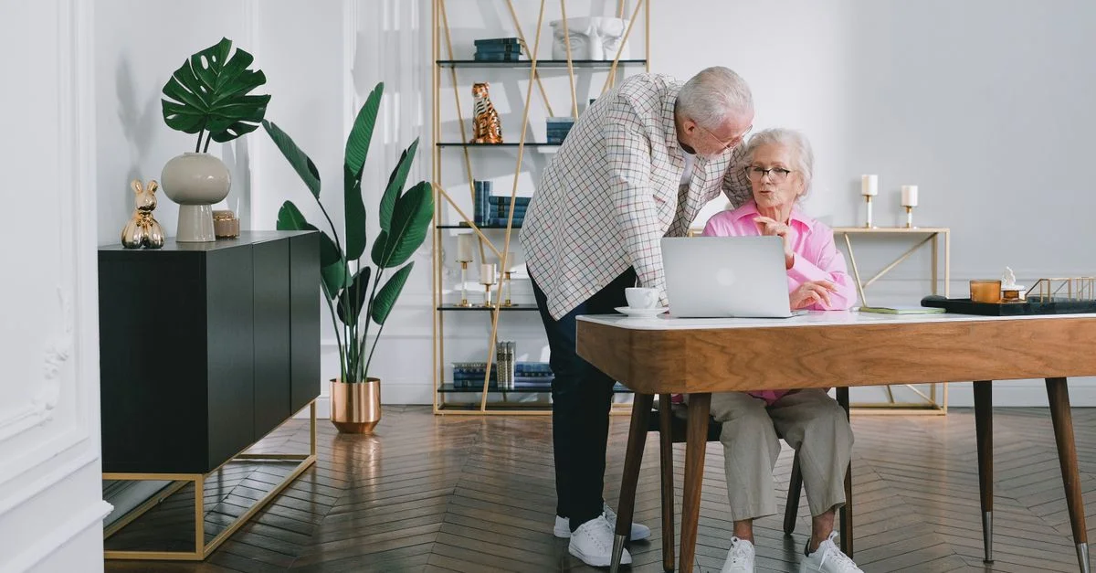 Un couple senior utilisant un ordinateur portable tout en discutant de quelque chose dans leur salon moderne.