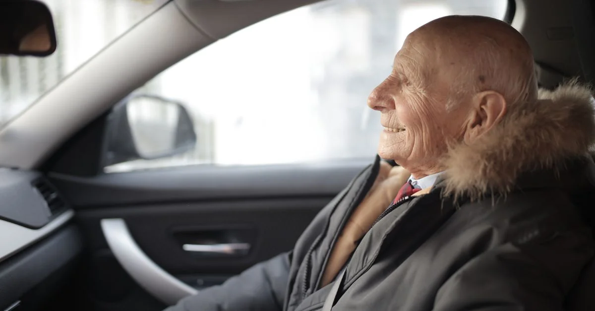 Un homme senior souriant confortablement assis à l'intérieur d'une voiture, profitant de sa conduite par une journée d'hiver.